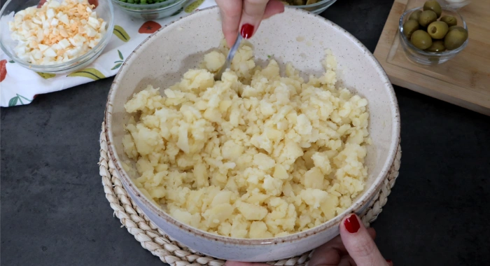 Patata cocida troceada y chafada con un tenedor en un bol amplio, con textura rústica, para la ensaladilla rusa