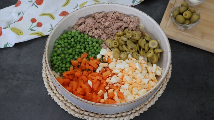 Bol con atún, guisantes, aceitunas laminadas, zanahoria en dados y huevo picado antes de mezclar la ensaladilla rusa