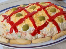 Ensaladilla rusa casera decorada con enrejado de pimiento rojo, yema de huevo desmenuzada, aceitunas y colines alrededor