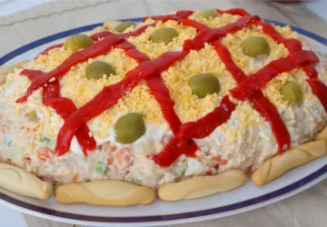 Ensaladilla rusa casera decorada con enrejado de pimiento rojo, yema de huevo desmenuzada, aceitunas y colines alrededor