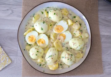 Vista cenital de una fuente de huevos en salsa de mostaza con patatas y perejil picado
