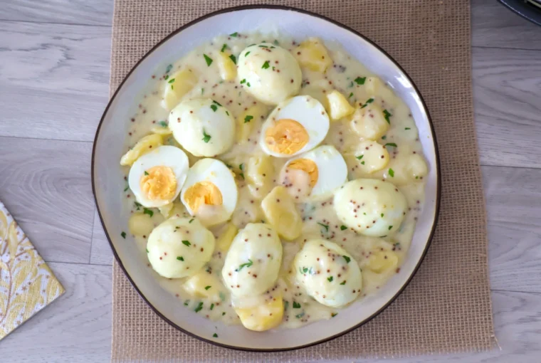 Vista cenital de una fuente de huevos en salsa de mostaza con patatas y perejil picado