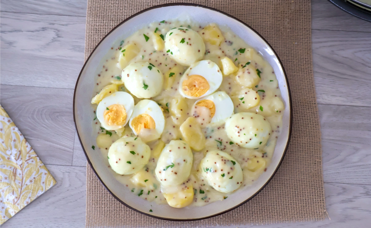 Vista cenital de una fuente de huevos en salsa de mostaza con patatas y perejil picado