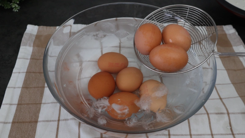 Huevos cocidos pasando a un bol con agua fría y hielo con ayuda de una espumadera