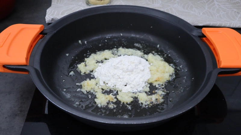 Harina incorporada sobre la cebolla pochada en mantequilla para formar el roux de la salsa