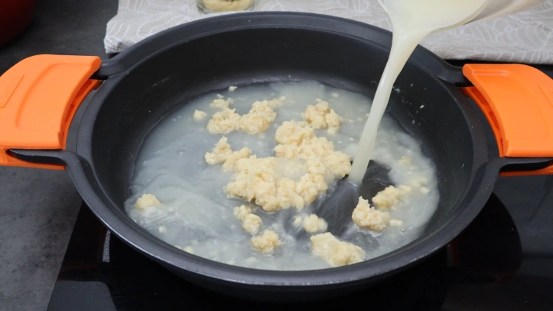 Añadiendo el caldo al roux, con la mezcla todavía sin integrar del todo en la cazuela