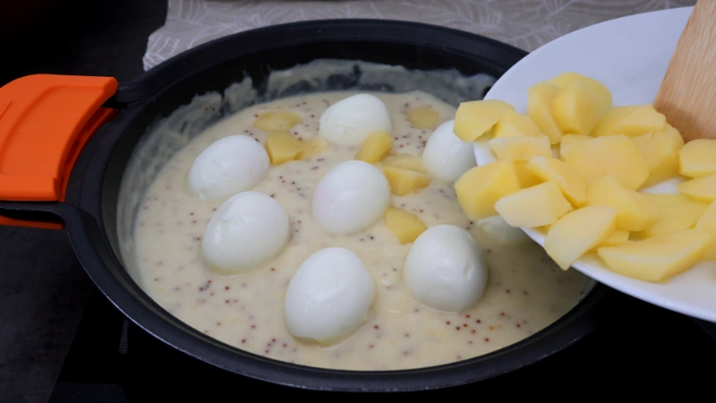 Huevos cocidos en la salsa de mostaza mientras se incorporan las patatas cocidas desde un plato