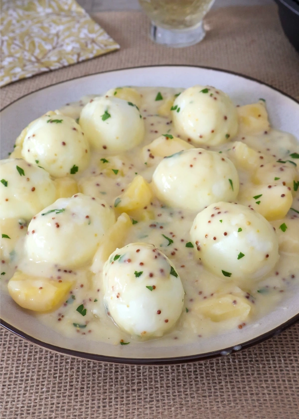 Fuente de huevos cocidos enteros en salsa cremosa de mostaza con patatas