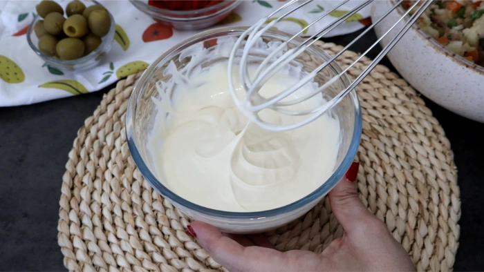 Mayonesa aligerada batida con unas varillas en un cuenco de cristal para la ensaladilla rusa