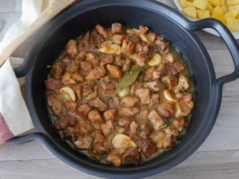 Cazuela con carne de cerdo al ajillo recién cocinada y servida junto a plato de patatas