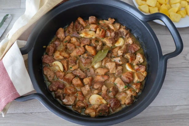 Cazuela con carne de cerdo al ajillo recién cocinada y servida junto a plato de patatas