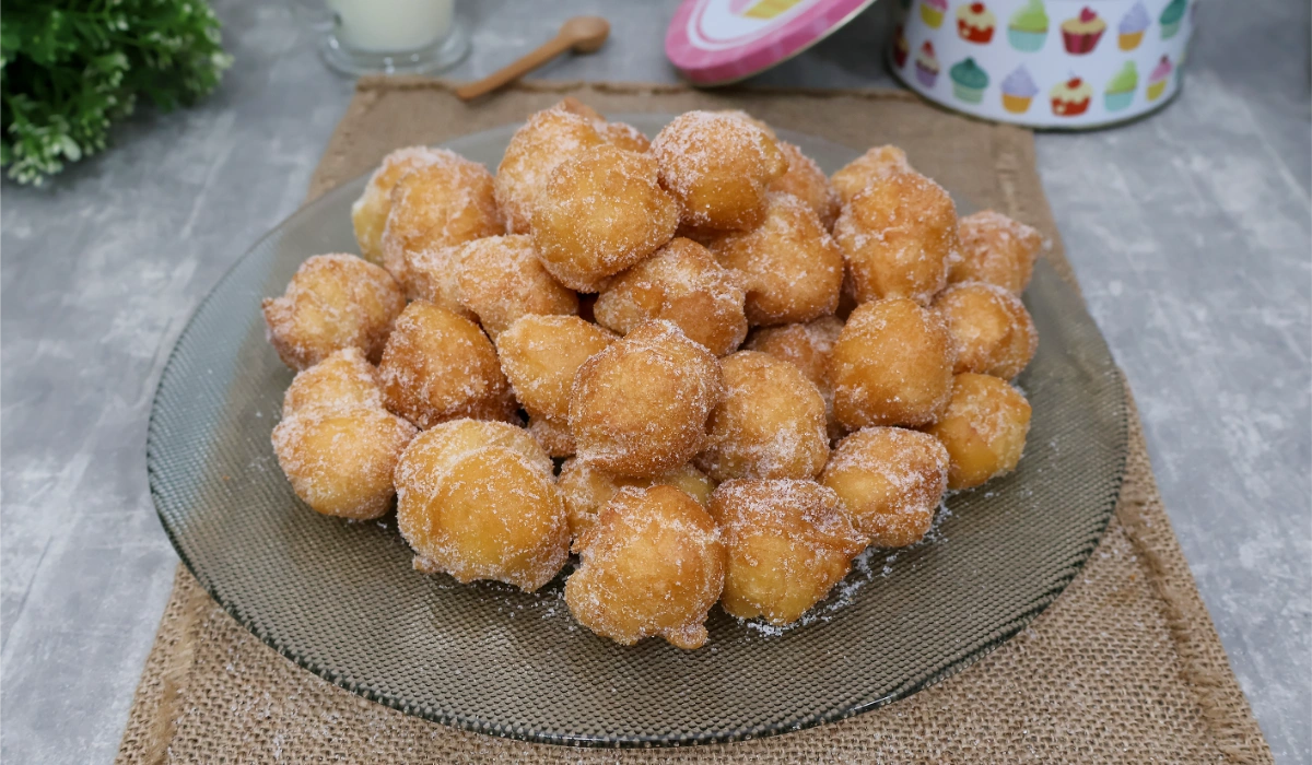 Buñuelos de viento caseros en un plato de cristal, con un vaso de leche al fondo