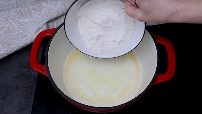 Añadiendo la harina al agua y la mantequilla calientes para hacer la masa de buñuelos de viento
