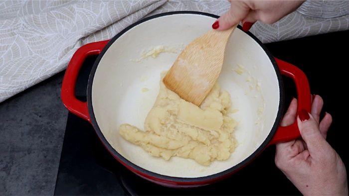 Masa de buñuelos cociéndose en la cazuela roja, removida con espátula de madera