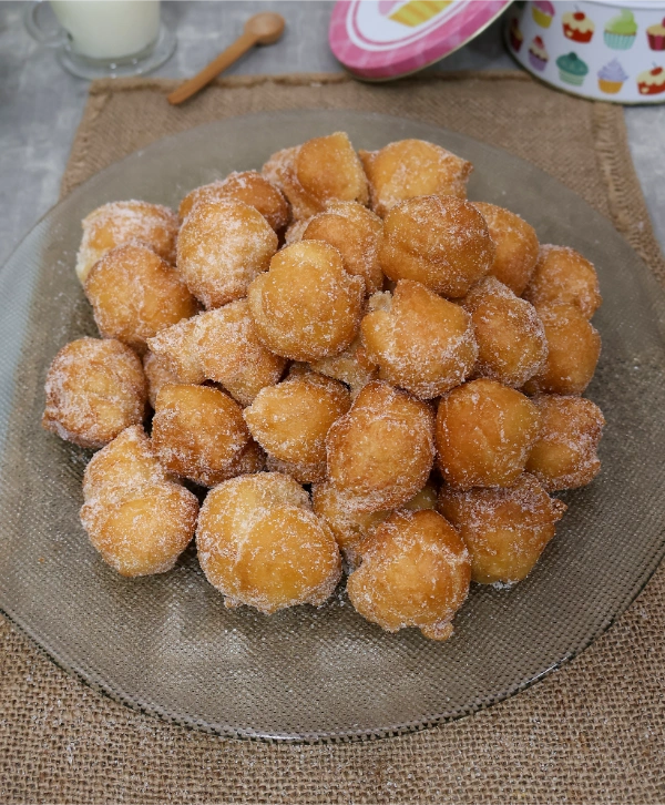 Plato de buñuelos de viento caseros rebozados en azúcar, apilados sobre un salvamanteles de yute